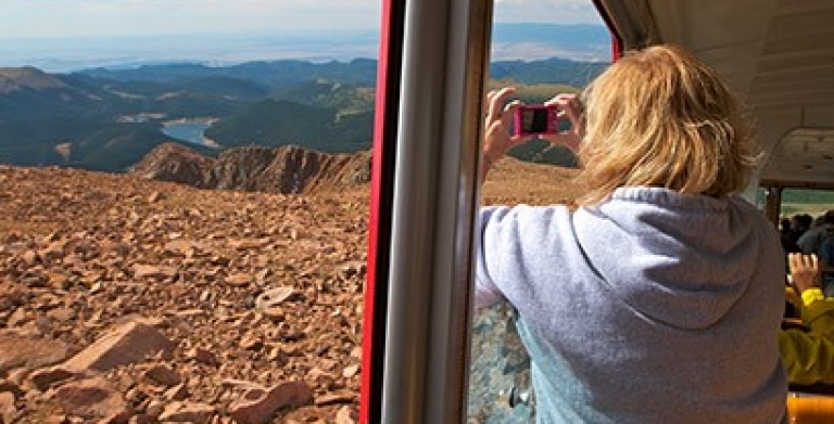 A woman taking a photo out of the window of a train.