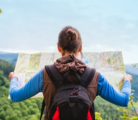 Hiking woman traveler with backpack checks map to find directions in wilderness area, real explorer. Travel Concept