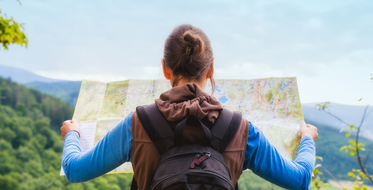 Hiking woman traveler with backpack checks map to find directions in wilderness area, real explorer. Travel Concept