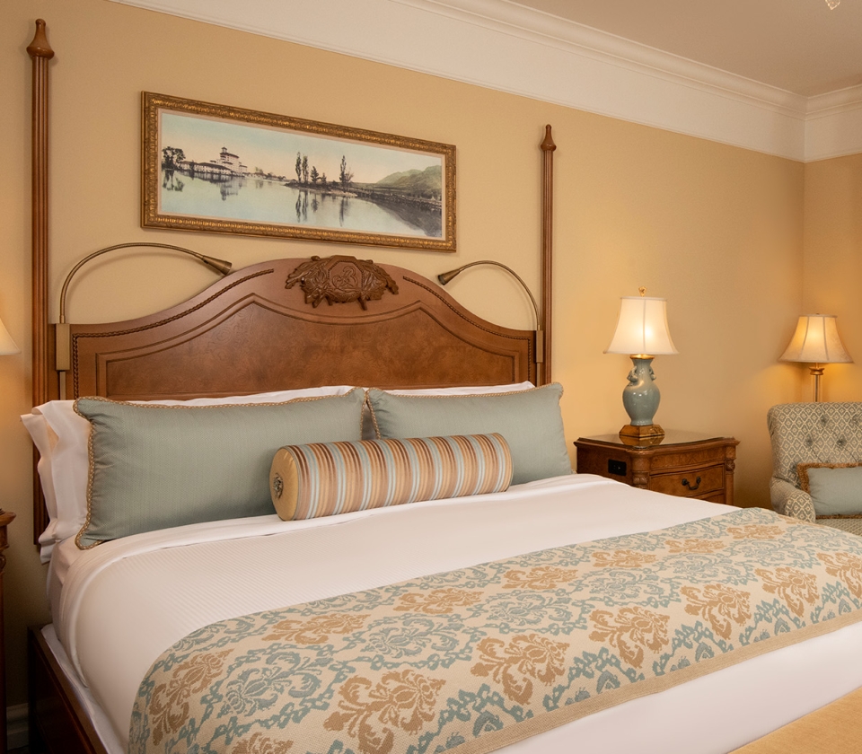 Interior king bed with yellow wallpaper and nicely made sheets
