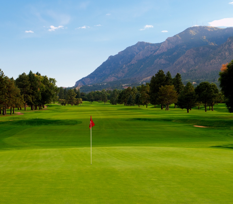 Golf green with red flagstick and mountains in background